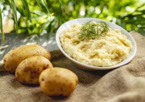 side view of mashed potatoes with dill in a white bowl on rustic background